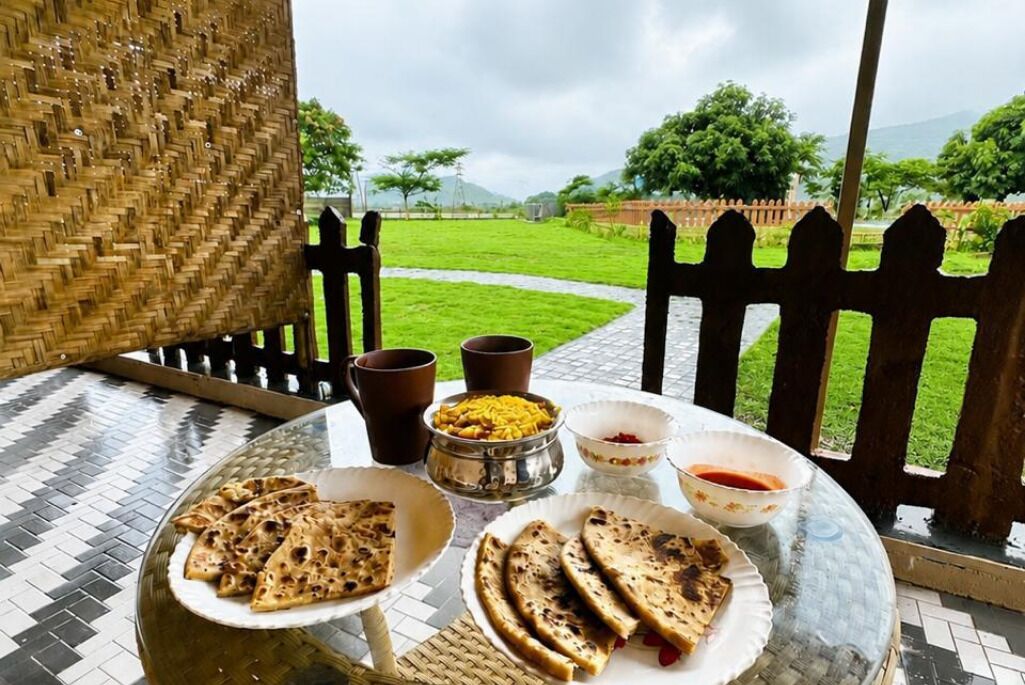 A table with food and drinks, a woven chair, and a view of a green landscape.