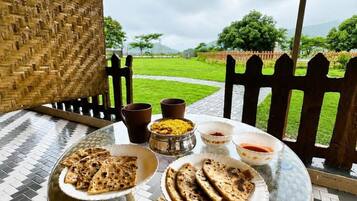 A table with food and drinks, a woven chair, and a view of a green landscape.