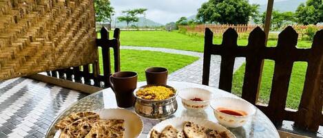 A table with food and drinks, a woven chair, and a view of a green landscape.