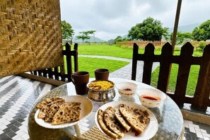 A table with food and drinks, a woven chair, and a view of a green landscape.