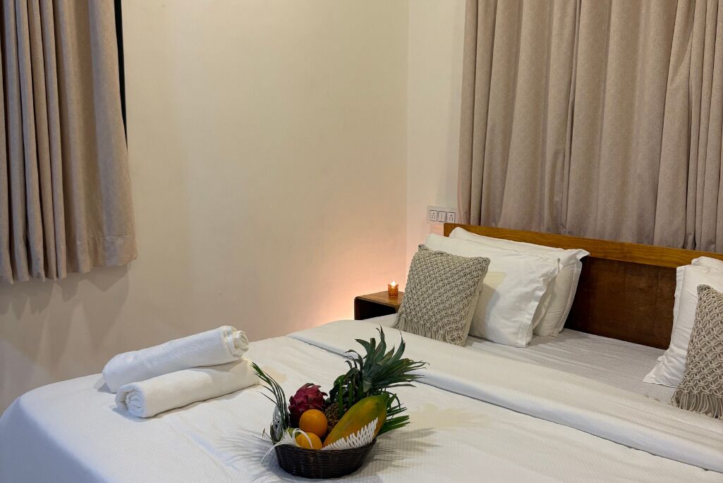 Een hotelkamer met een net opgemaakt bed, een fruitmand op het bed en een nachtkastje met een kaars.