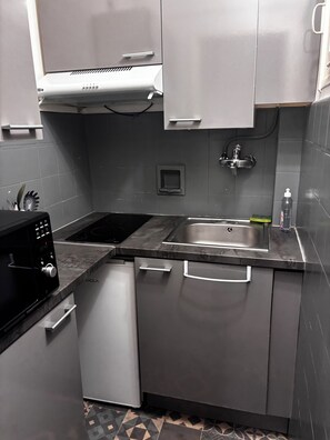 Eine kompakte Küche mit eingebauter Mikrowelle, einem Geschirrspüler, einer Edelstahl-Spüle und einem kleinen Fenster.