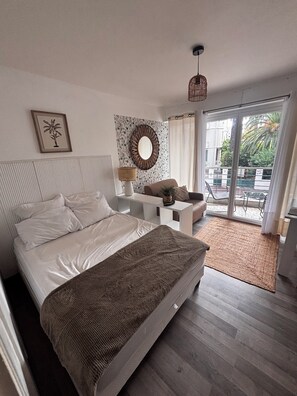 Ein Schlafzimmer mit einem Bett, einem Nachttisch, einer Lampe, einem Spiegel und Blick ins Freie.