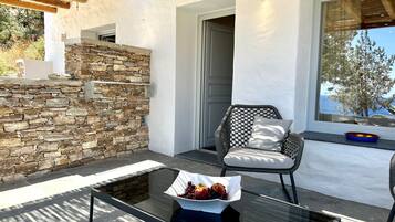 Un espace extérieur moderne, aménagé avec un mur en pierre, une table en verre ornée de fruits et un fauteuil en osier.