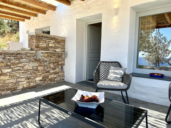 A modern outdoor seating area with a stone wall, a glass table with fruit, and a wicker chair.
