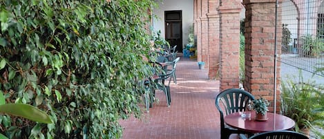 A covered patio area with brick flooring, green foliage, and outdoor furniture.