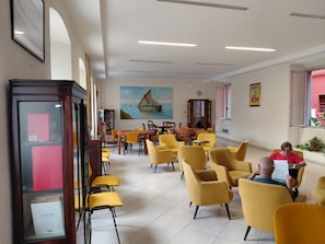 A spacious indoor area with yellow chairs arranged around tables, a large painting of a sailboat on the wall, and a red structure on the left. - VILLA GLAUER - D'AMICO (Sestri Levante)