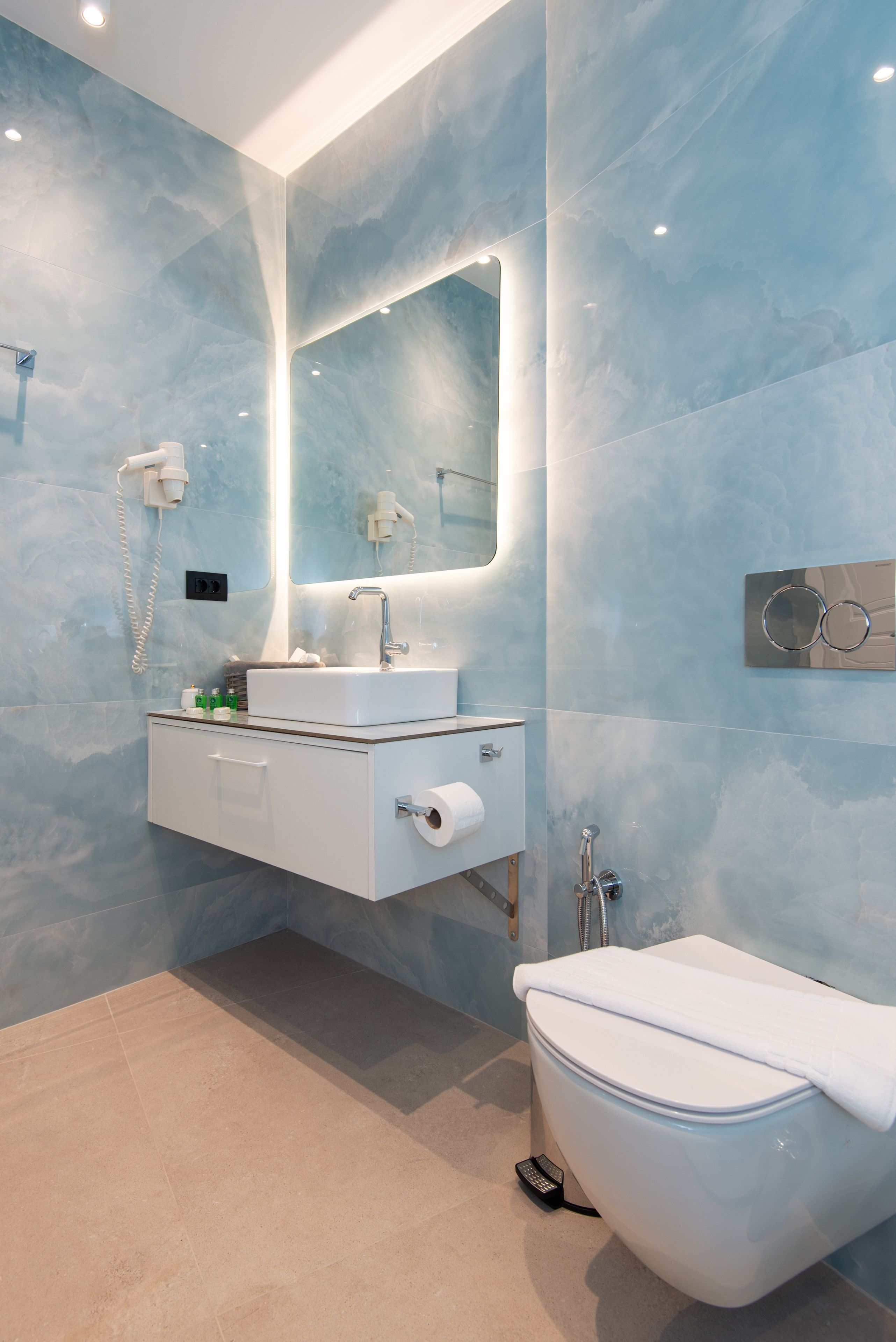 Une salle de bain moderne avec un mur en marbre, un lavabo blanc, un miroir, des toilettes et une douche.