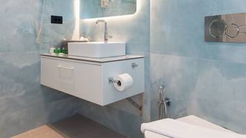 Une salle de bain moderne avec un mur en marbre, un lavabo blanc, un miroir, des toilettes et une douche.