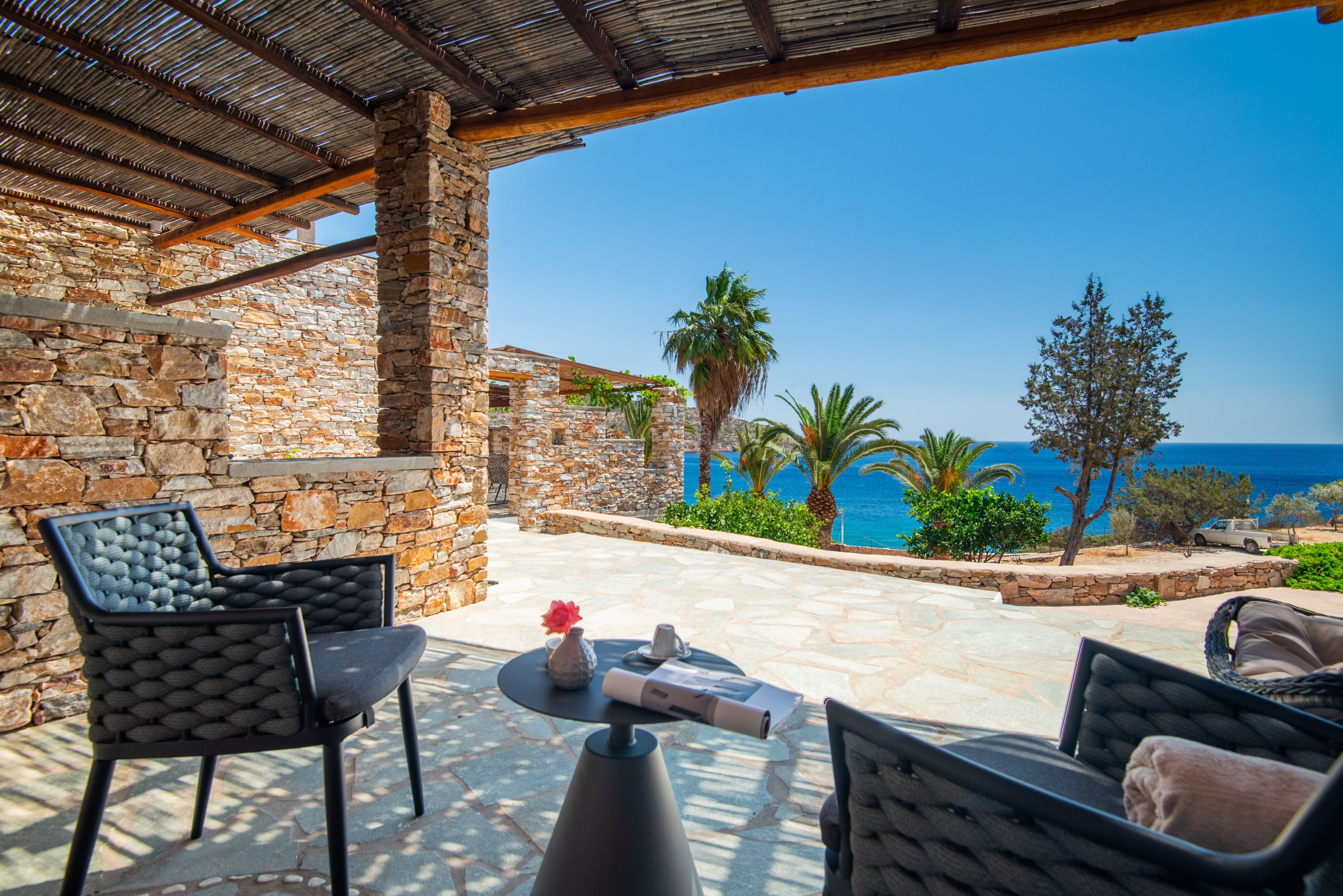 Une terrasse en pierre avec des meubles d’extérieur, une vue sur la mer et un ciel dégagé.