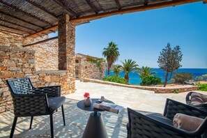 A stone patio with outdoor furniture, a view of the sea, and a clear sky.