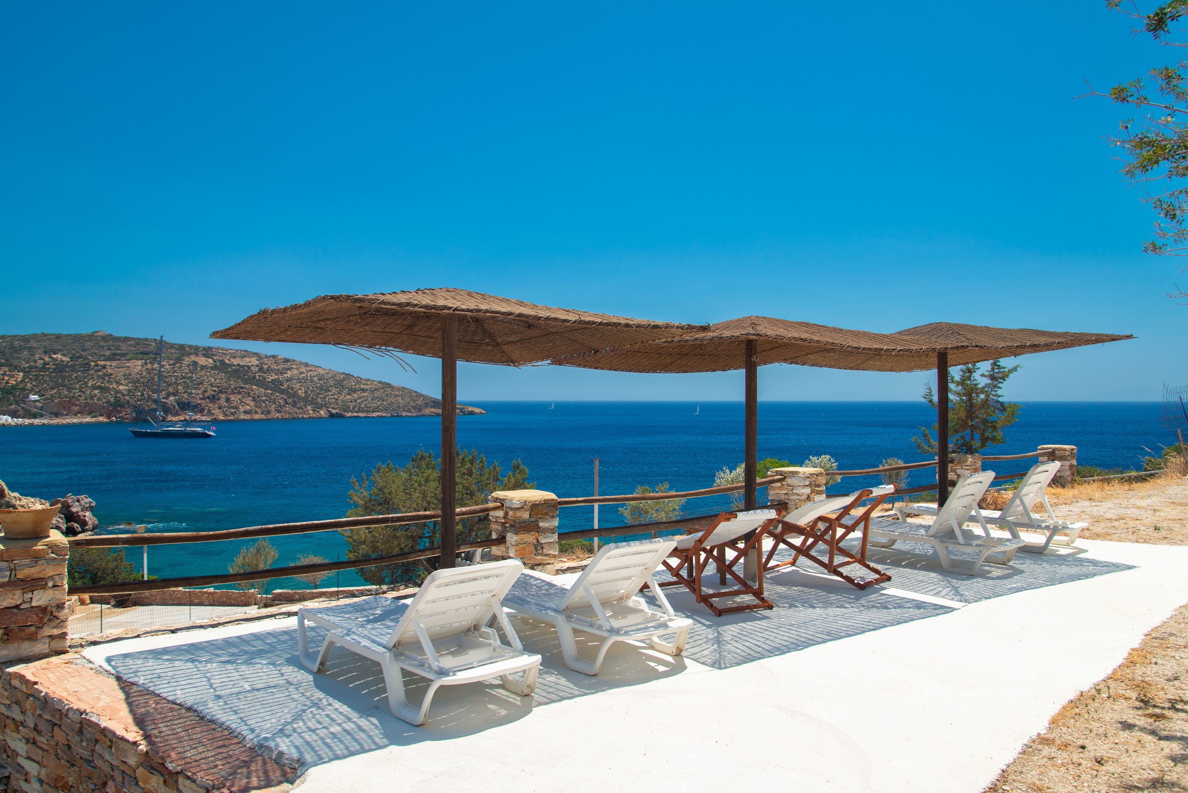 Eine Strandterrasse mit weißen Liegestühlen und Strohdächern, mit Blick auf das klare blaue Meer und das entfernte Land.