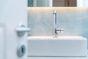 A modern bathroom with a sleek, chrome faucet mounted on a white sink. - White & Black Suites – Suite Two (Lazarou beach bay)
