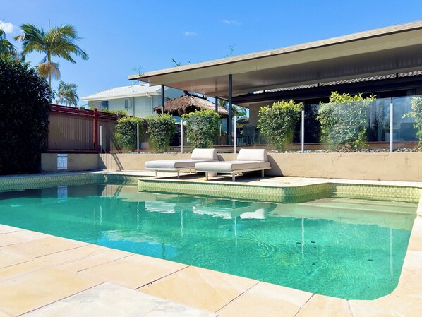 A swimming pool with a lounge area, surrounded by a modern house with a covered patio. - Waterfront Retreat with Pool & Pontoon, Broadbeach (Broadbeach Waters)