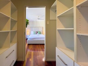 A hotel room with a bed, a ceiling fan, and a hallway leading to a closet with shelves. - Waterfront Retreat with Pool & Pontoon, Broadbeach (Broadbeach Waters)