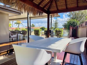 Une terrasse extérieure dotée d’un toit de chaume, de tables et de chaises blanches.
