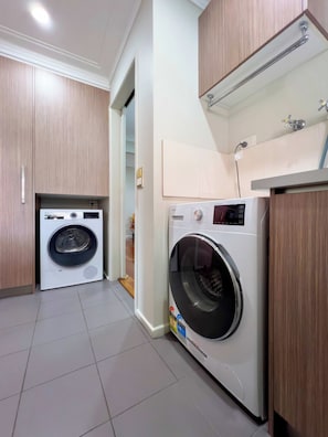 A laundry room with two washing machines, wooden cabinets, a tiled floor, and a small sink area. - Waterfront Retreat with Pool & Pontoon, Broadbeach (Broadbeach Waters)