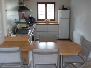 A compact kitchen with a dining table and chairs, a refrigerator, and a window with blinds. - Small house 2 km from the sea (villeneuve-Loubet)