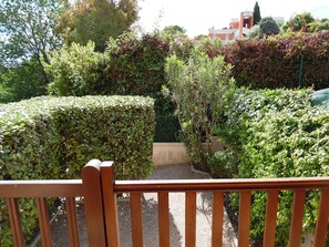 A wooden bench in a garden with various shrubs and a building in the background. - Small house 2 km from the sea (villeneuve-Loubet)