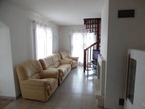 A living room with a beige sofa, a television on a stand, and a staircase leading to an upper floor. - Small house 2 km from the sea (villeneuve-Loubet)