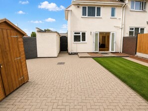A residential property with a paved patio, a wooden gate, and a well-maintained lawn. - House Sleeps 4 With Parking (Sutton Coldfield)