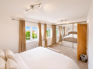 A bedroom with a large bed, a wooden door, and a view of a garden through the window. - House Sleeps 4 With Parking (Sutton Coldfield)