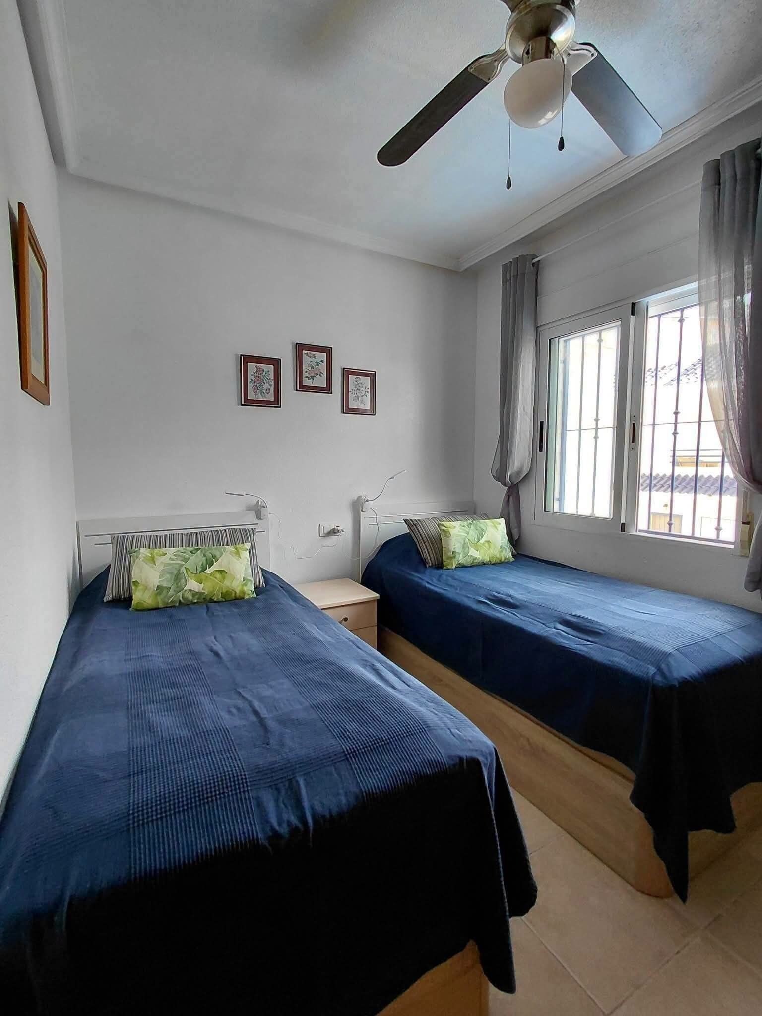 A room with two beds, a ceiling fan, and a window with curtains.