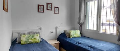Quarto com duas camas, ventilador de teto e janela com cortinas.