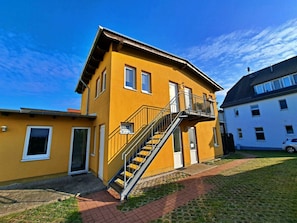 A two-story yellow building with a staircase leading to a balcony, adjacent to a white building. - Holiday Apartment With 1 Bedroom (Heringsdorf)