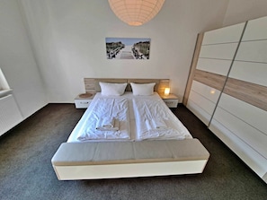 A double bed with a headboard, bedside tables, a wall-mounted lamp, and a framed picture above the bed. - Holiday Apartment With 1 Bedroom (Heringsdorf)