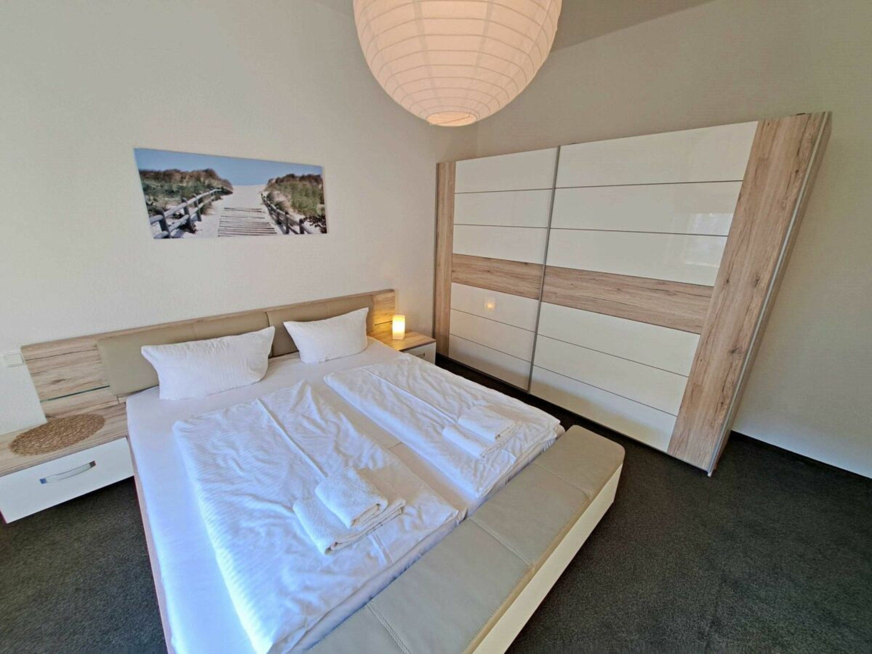 Un dormitorio con cama, mesita de noche, luz de pared y una ventana grande.