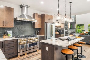 A modern kitchen with a central island, stainless steel appliances, and a herringbone-patterned backsplash.