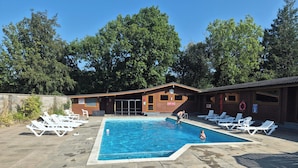 A swimming pool with lounge chairs, a wooden building with a clock, and a lifebuoy.