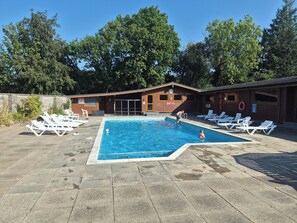 Piscina com espreguiçadeiras, prédio de madeira com relógio e boia.