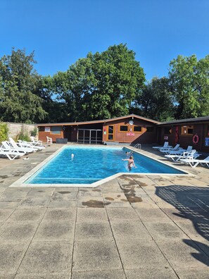 En swimmingpool med liggestole og en træbygning med et skilt.