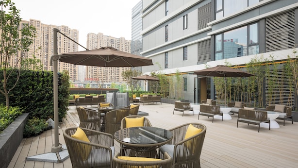 An outdoor patio area with wicker furniture, umbrellas, and a view of high-rise buildings. - The Mulian Hotel (Chengdu)