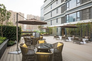 Un patio al aire libre con mobiliario de mimbre, sombrillas y vistas a edificios altos.