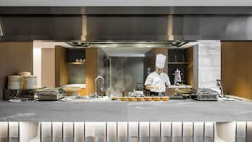 A modern kitchen with stainless steel appliances, a chef preparing food, and a bar area with glasses and bottles.