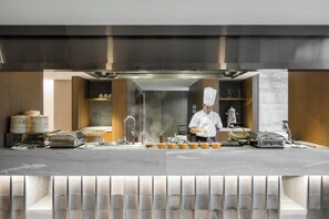 Una cocina moderna con electrodomésticos de acero inoxidable, un chef preparando comida y una zona de bar con vasos y botellas.