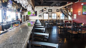 A bar area with a long counter, multiple seating options, and a television screen displaying a sports channel.