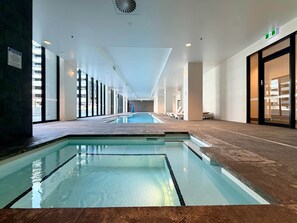A modern indoor swimming pool with clear water, surrounded by a tiled floor and walls, and a long corridor with seating areas. - Elegant Parkes Stay near Lake & Parliament (Parkes)