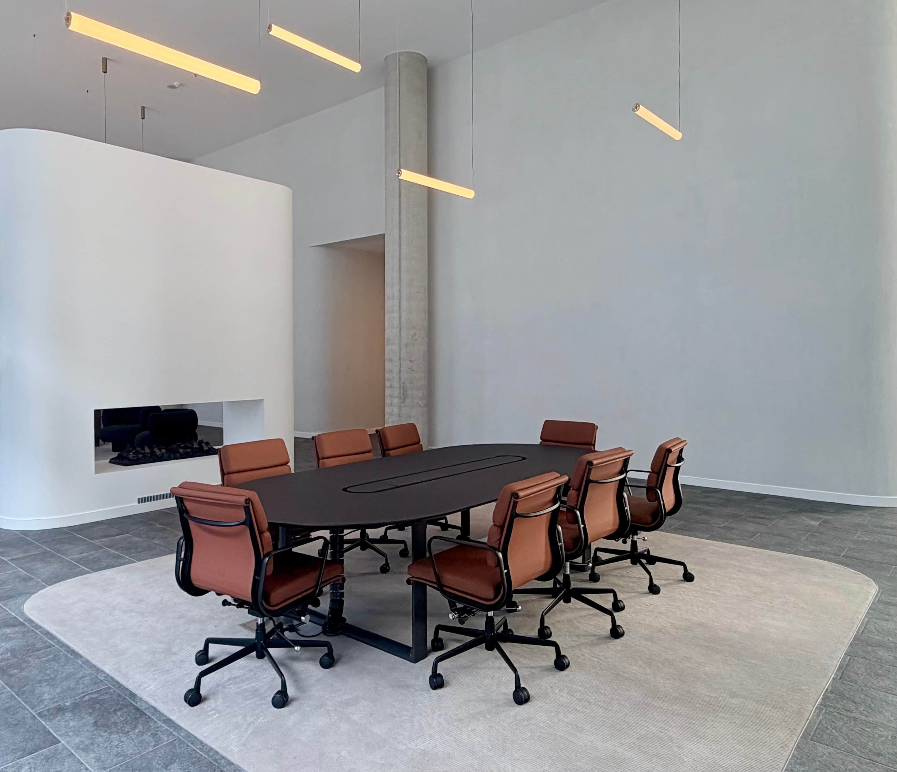 A modern conference room with a large table and eight chairs, a white accent wall, and pendant lighting.