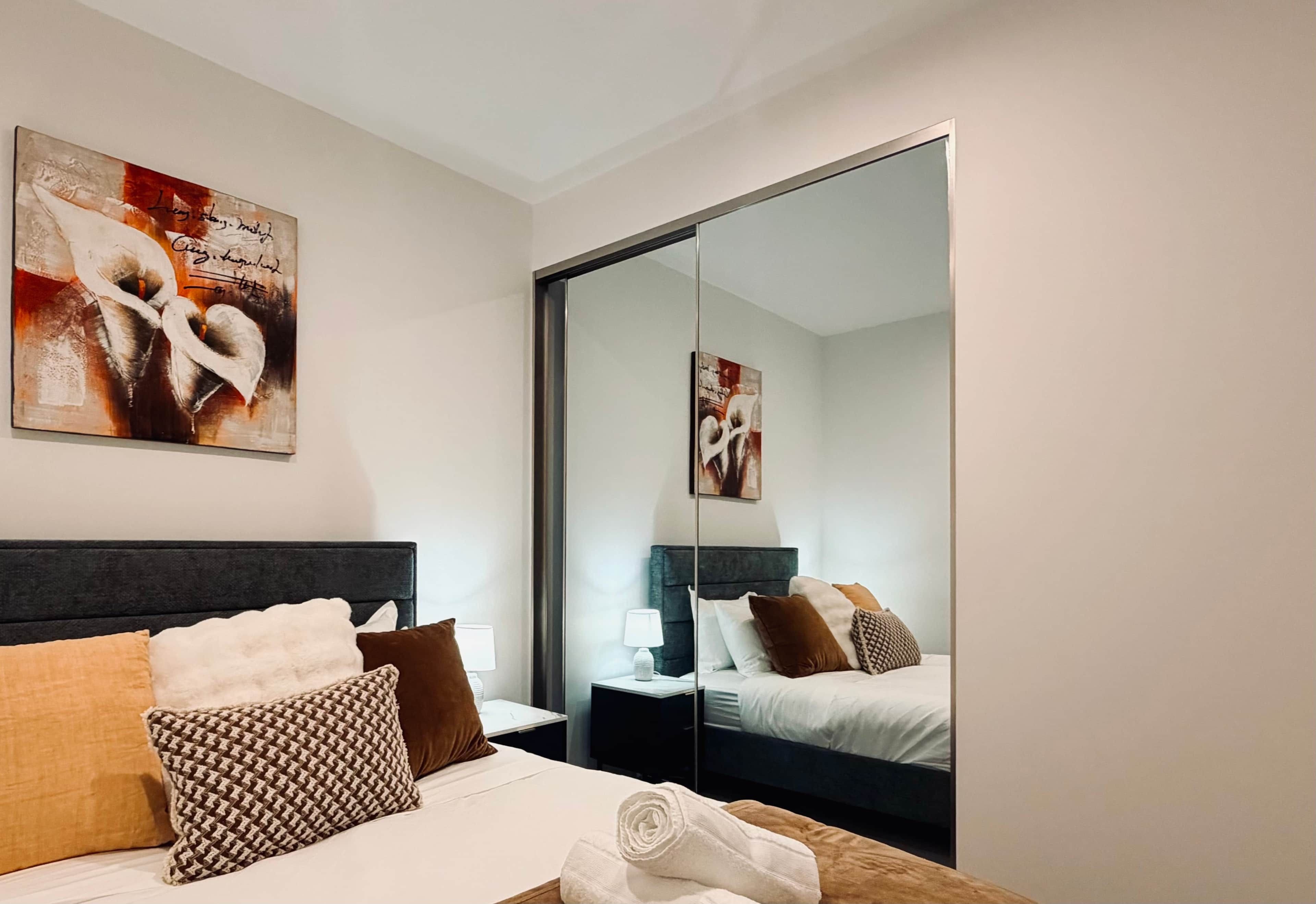 A hotel room with a bed, a nightstand, a lamp, a mirror, and artwork on the wall.