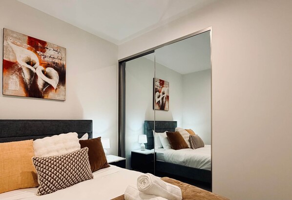 A hotel room with a bed, a nightstand, a lamp, a mirror, and artwork on the wall. - Elegant Parkes Stay near Lake & Parliament (Parkes)