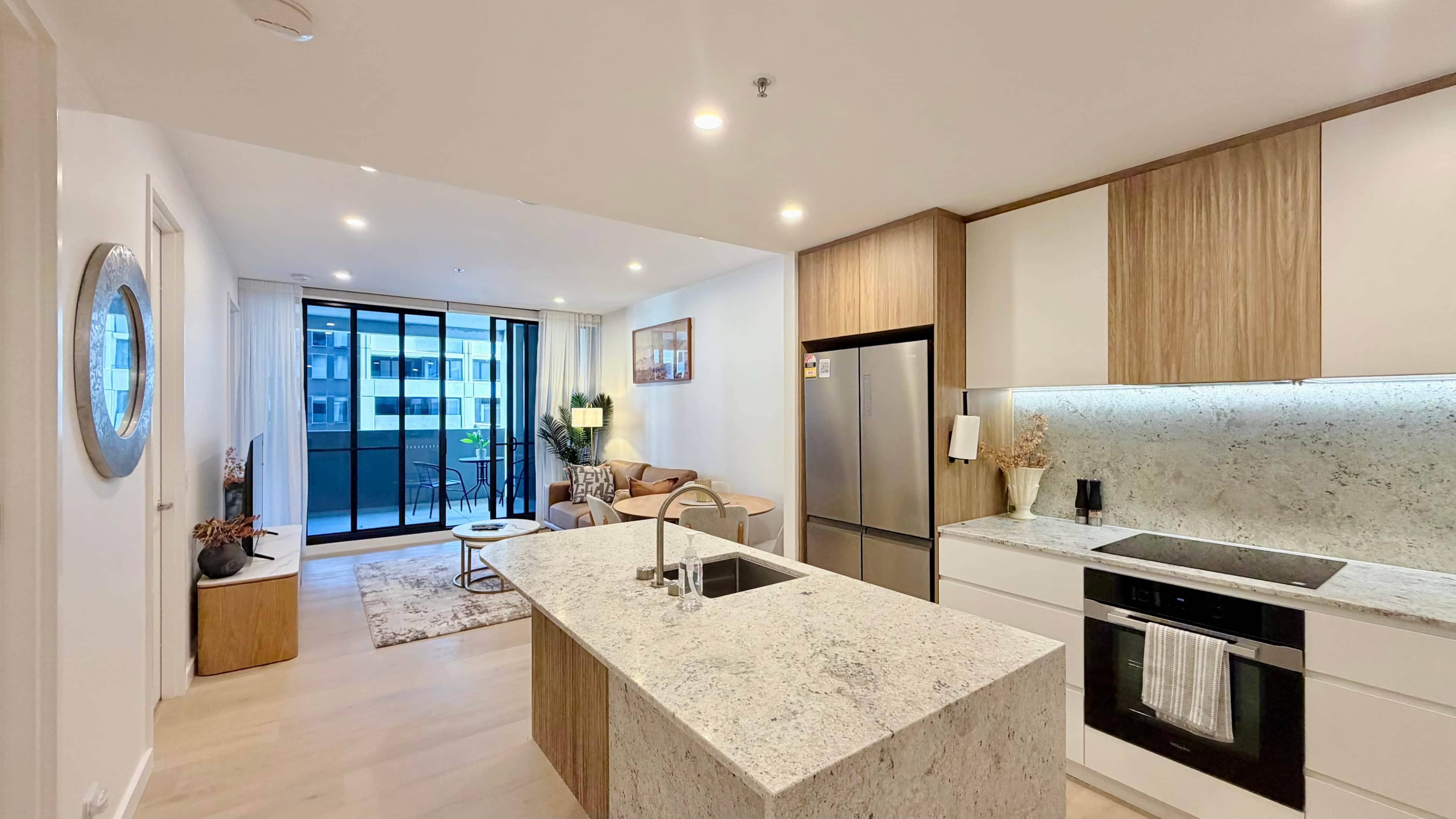 A modern kitchen with a central island, built-in appliances, and a view to a balcony.