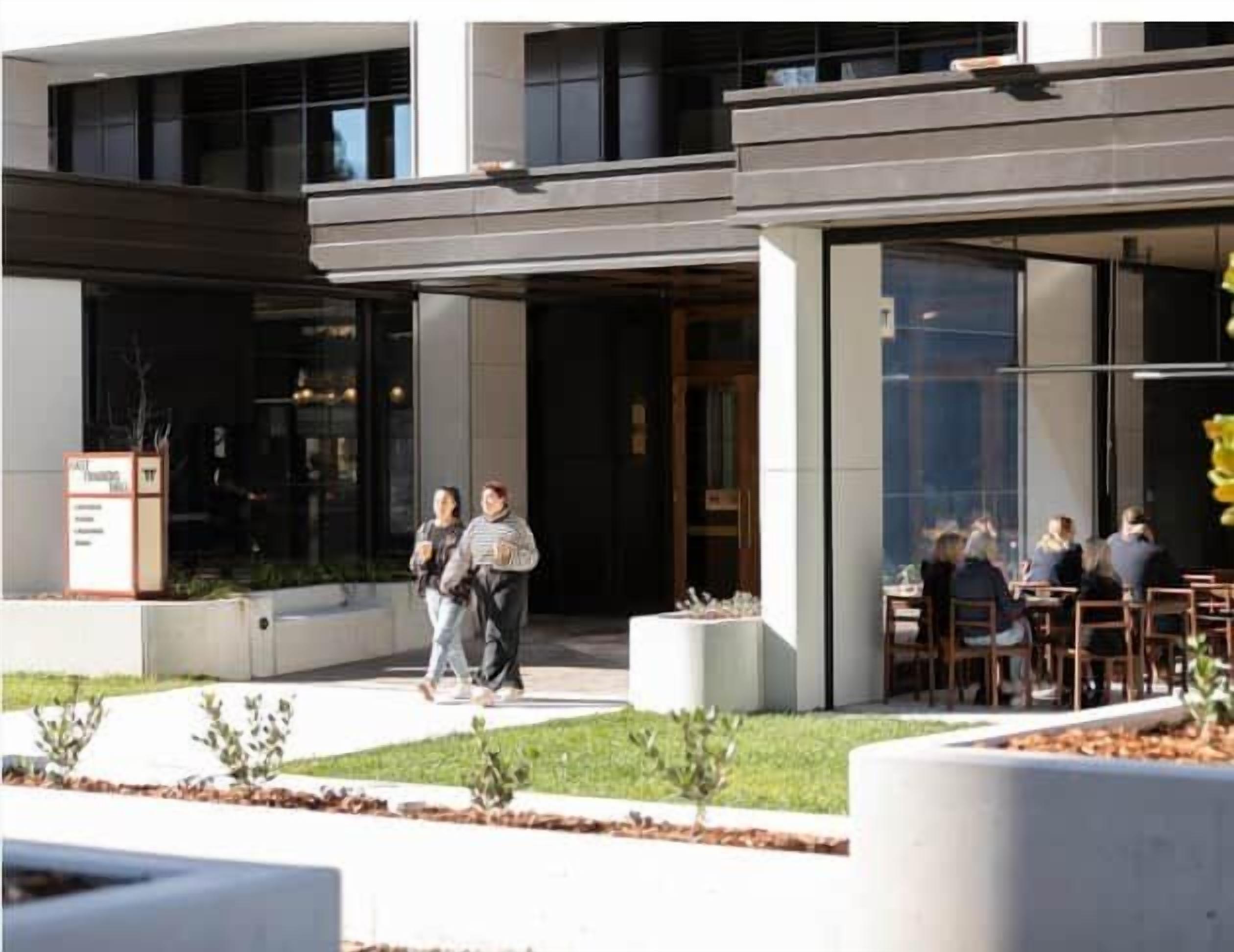 A modern building with a glass facade, outdoor seating area, and a planter with small plants.