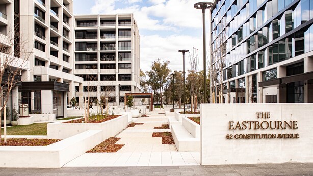 A modern building complex with multiple floors, a central open space with pathways, and a sign indicating 'The Eastbourne 62 Constitution Avenue.' - The Eastbourne Premium 2BR Central Canberra (Parkes)