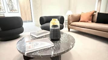A modern living room with a round coffee table, two black armchairs, a beige sofa, and a lamp.