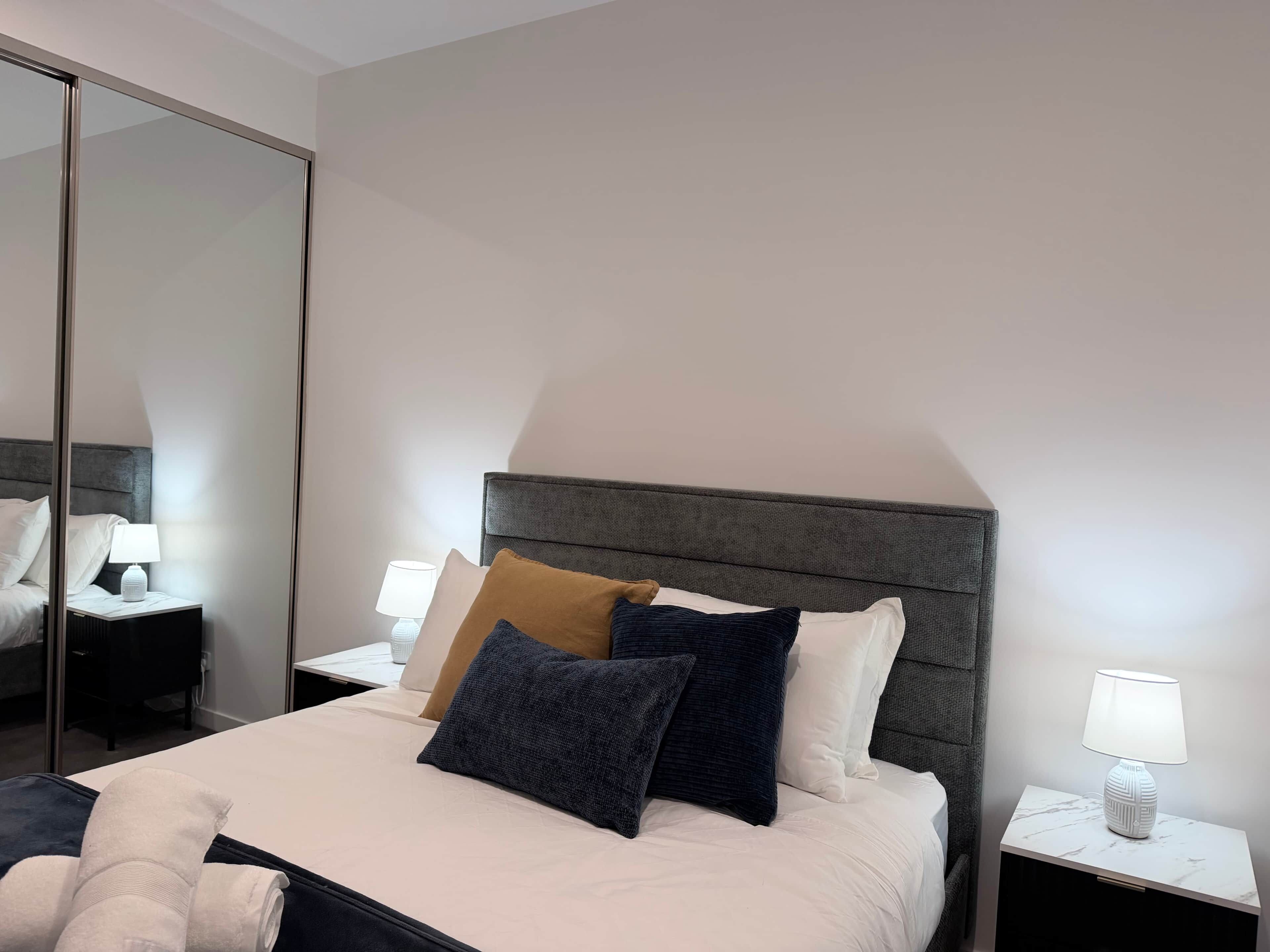A hotel room with a bed, nightstands, a lamp, and a mirror.
