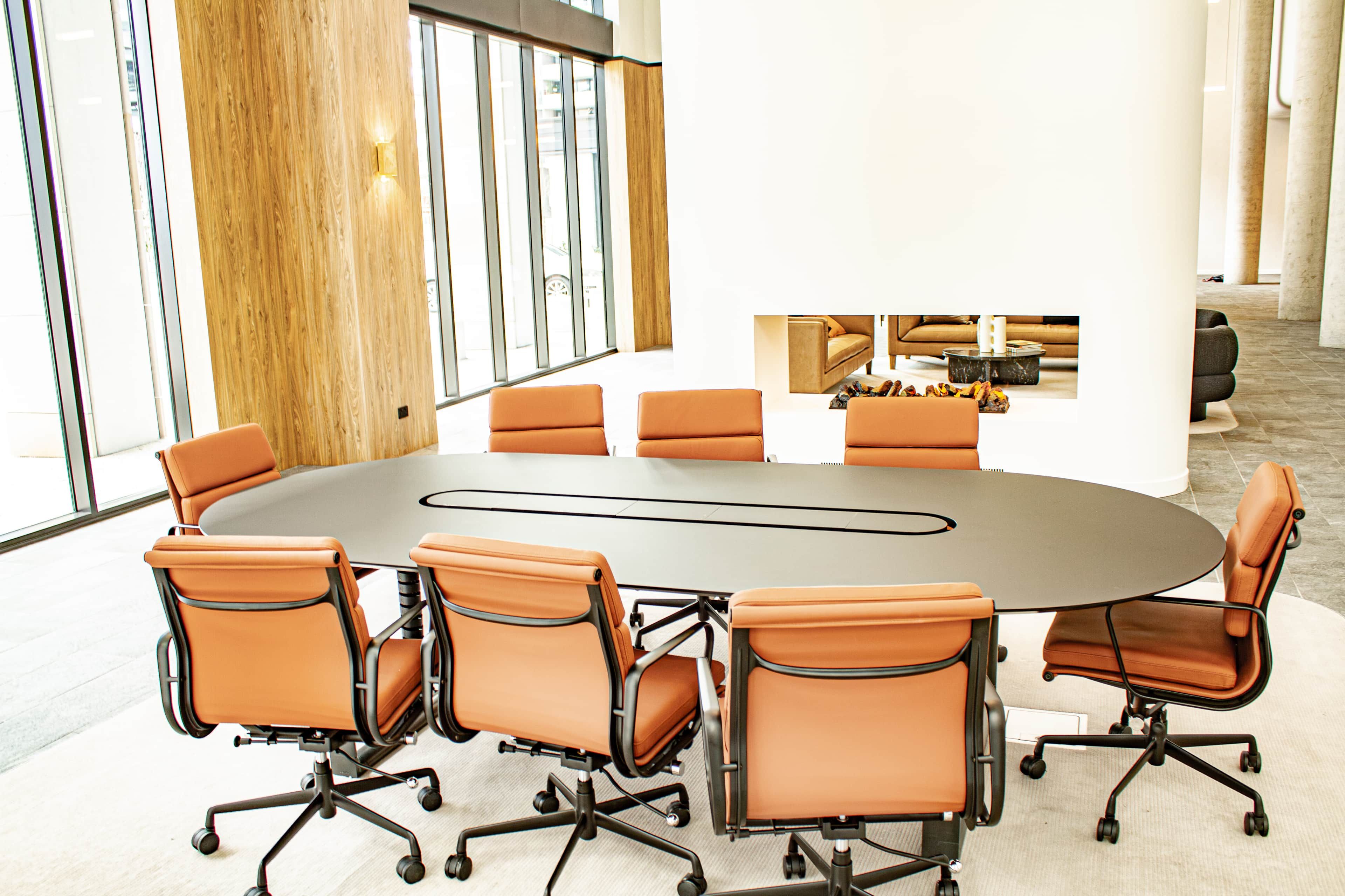 A conference room with a round table and six chairs, large windows, and a wooden accent wall.